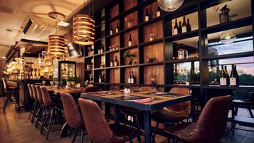 A restaurant with a long counter, multiple chairs, and a wine rack with bottles.