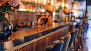 A bar area with a long counter, multiple bar stools, and hanging light fixtures. - Paris (Opatija)