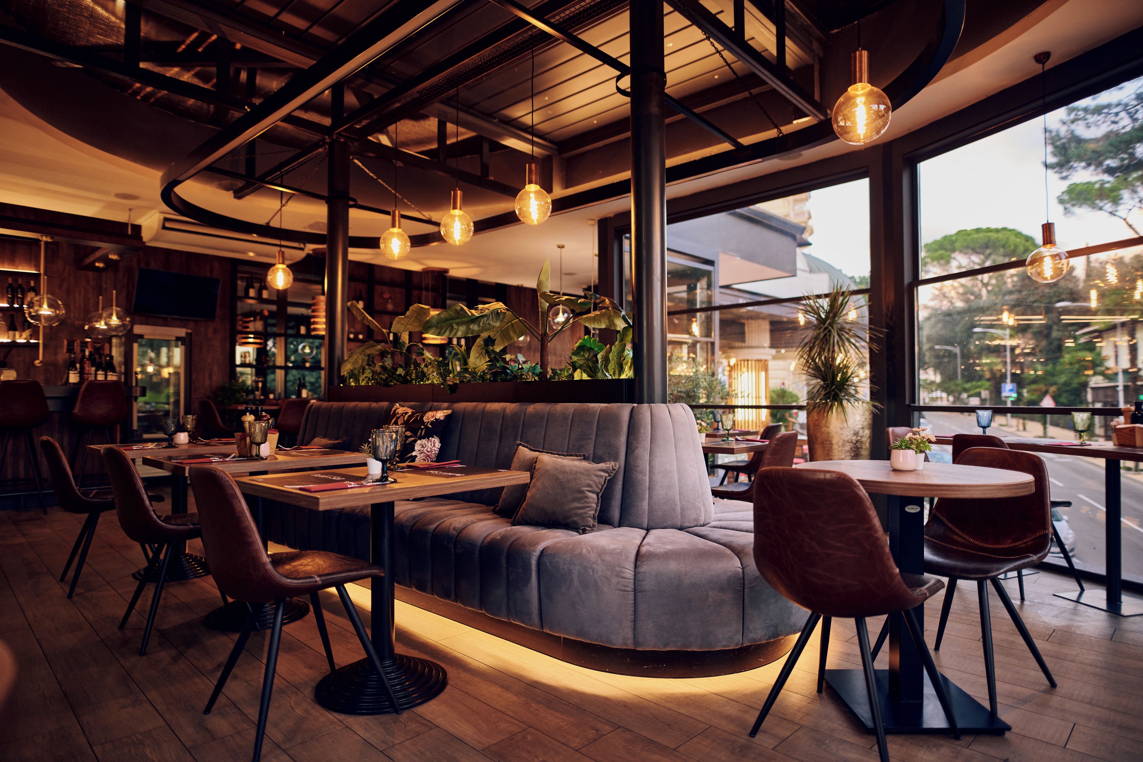 Een modern restaurantinterieur met een gebogen bank, ronde tafels en hangende pendellampen.