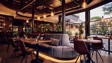 Een modern restaurantinterieur met een gebogen bank, ronde tafels en hangende pendellampen.