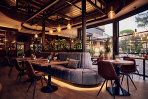 A modern restaurant interior with a curved sofa, round tables, and hanging pendant lights.
