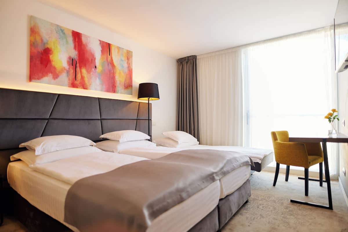 A hotel room with two beds, a desk, a chair, and a large abstract painting on the wall.