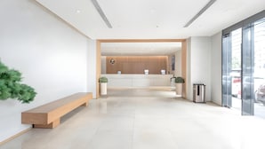 Un hall d’hôtel moderne avec un banc en bois, un comptoir d’accueil et une poubelle.