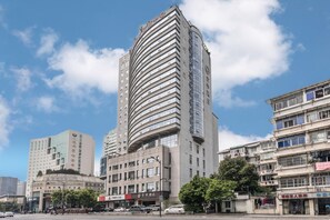 A multi-story hotel with a curved facade, several ground-level shops, and a clear sky. - Ji Hotel (Hangzhou)