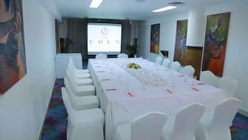Un salón de conferencias con una larga mesa, sillas blancas y una pantalla de proyector que muestra el logotipo de 'The Eden Resort & Spa'.