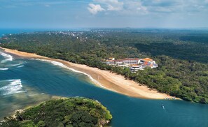 A coastal hotel with multiple buildings, beachfront access, and surrounding forested landscape.
