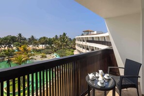 A balcony with a table set for tea, overlooking a pool and palm trees.