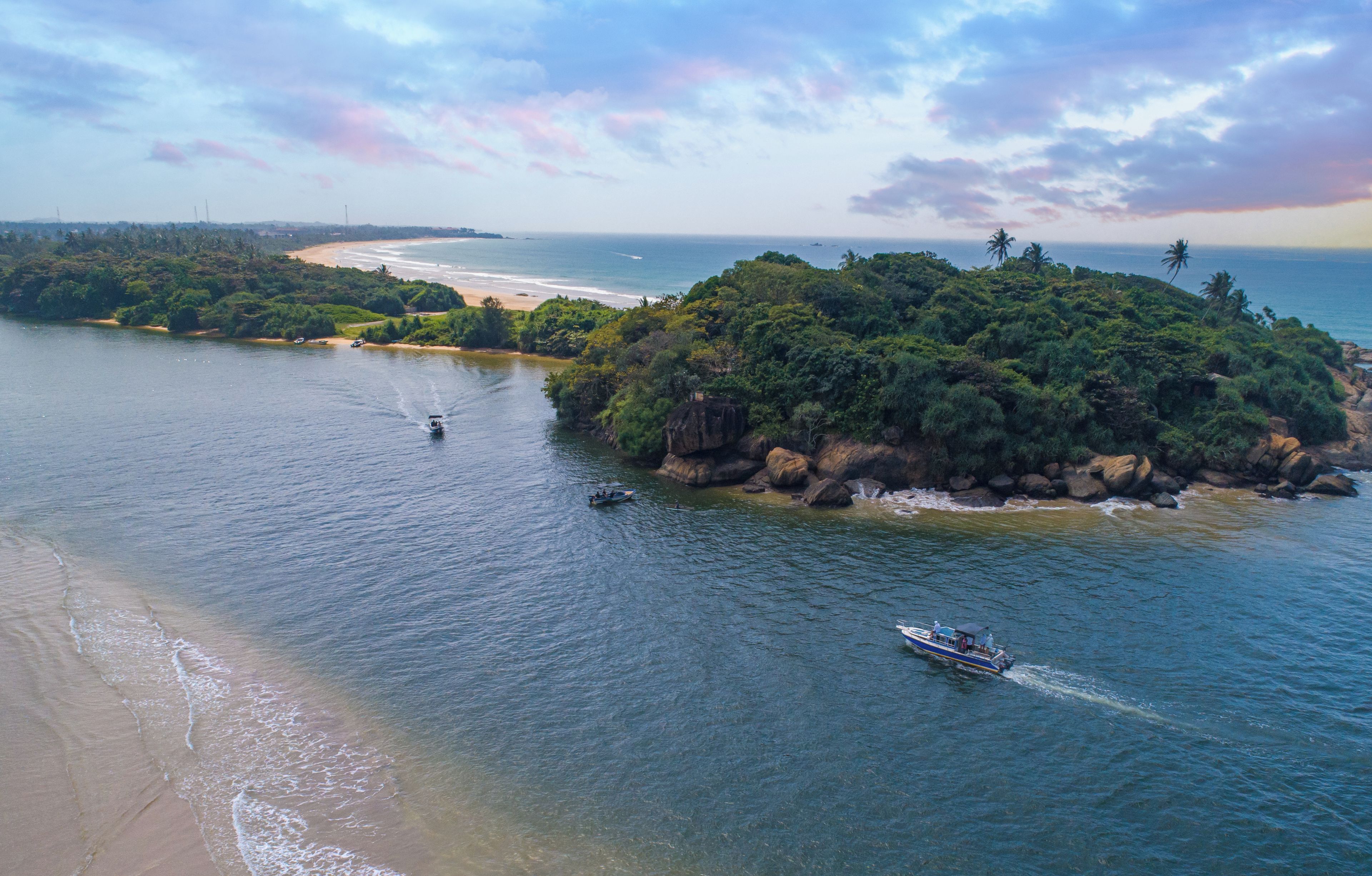 A coastal landscape with a beach, boats, and lush greenery.