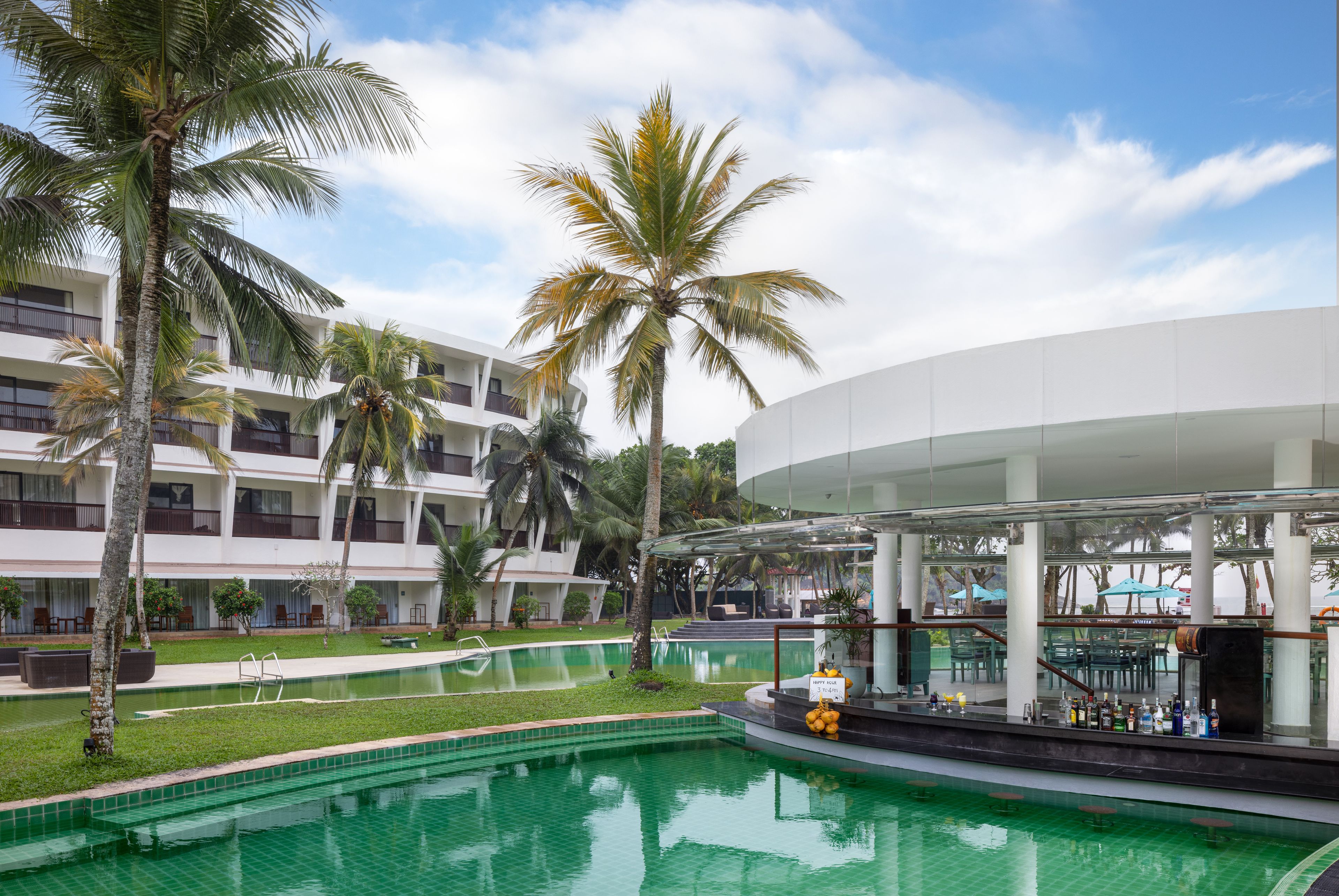 A hotel with a swimming pool, palm trees, and a bar area.