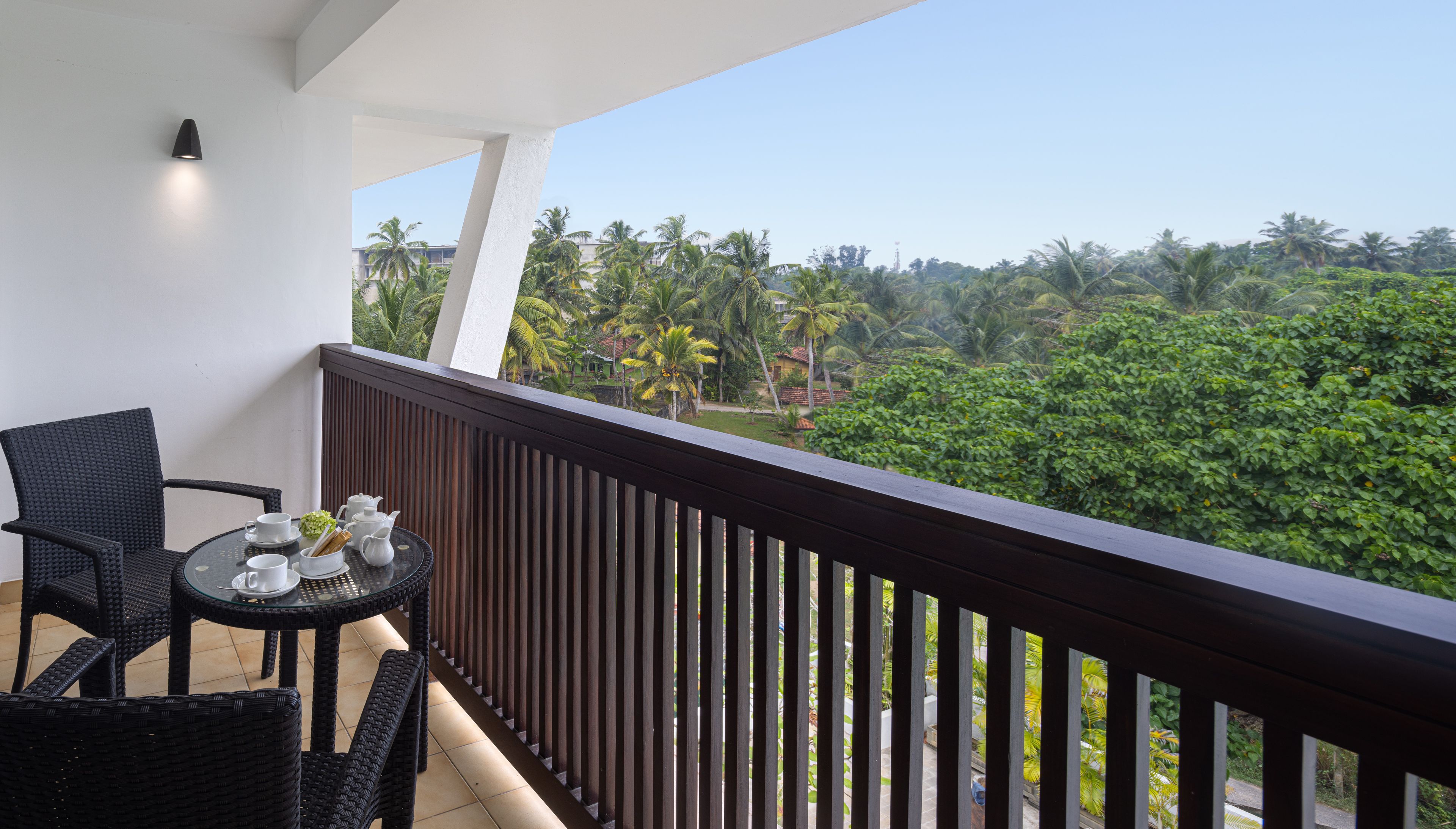 A balcony with a view of a lush green landscape, a table with a chair, and a small table with a teapot and cups.