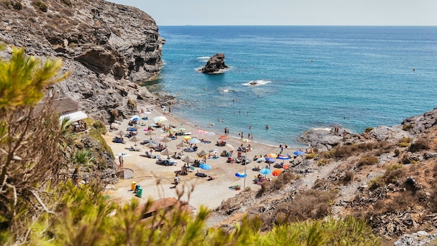 Une plage bordée de falaises rocheuses, avec une mer bleue et limpide, et des parasols.