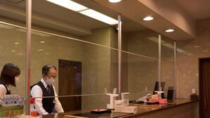 A reception desk with a glass partition, a digital screen, and a wooden counter.