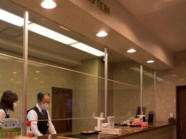 Un mostrador de recepción con un separador de vidrio, una pantalla digital y una encimera de madera.