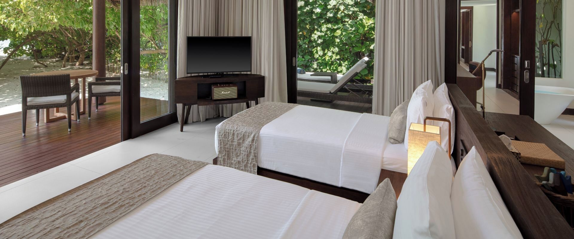 A hotel room with two beds, a TV, a small desk, and a view of the outdoors.