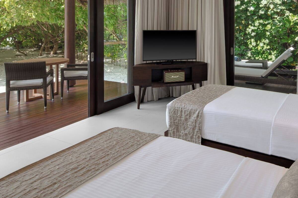 Quarto de hotel com duas camas, televisão, pequena mesa de trabalho e vista para o exterior.