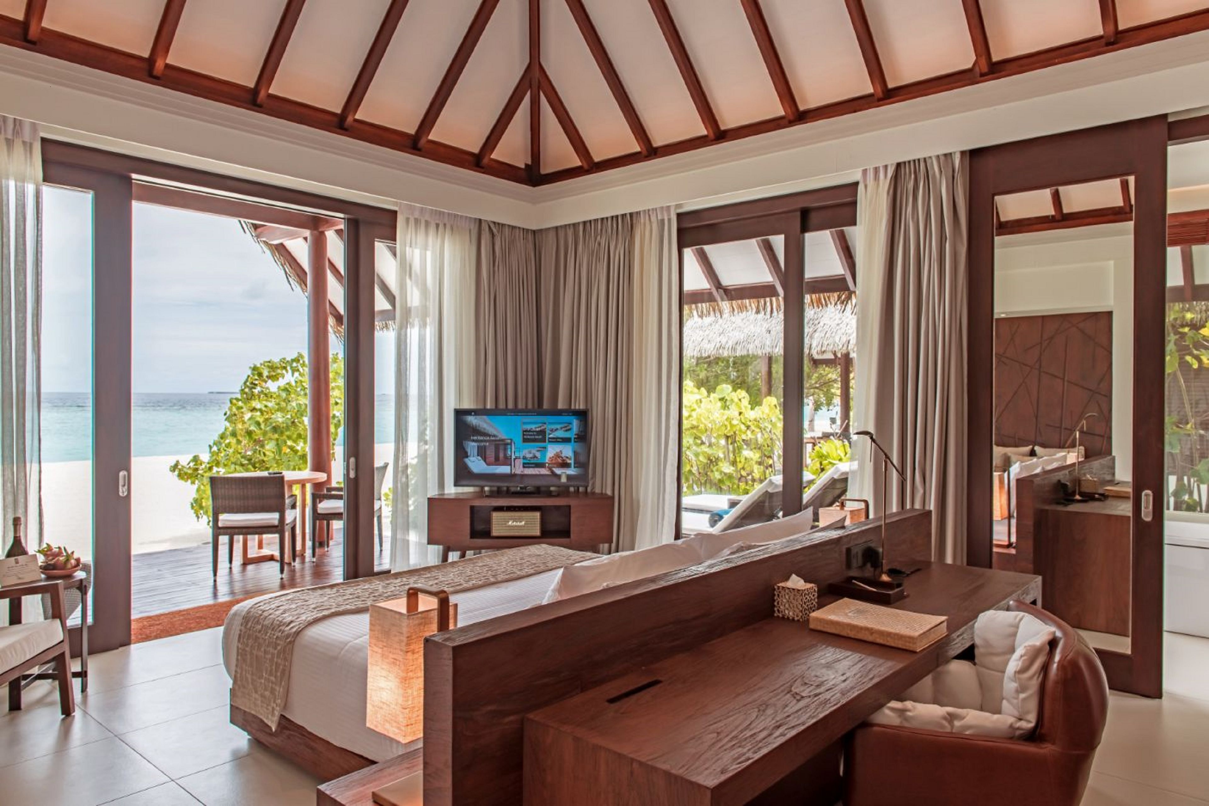 A bedroom with a large bed, a TV, a desk, and a view of the sea.