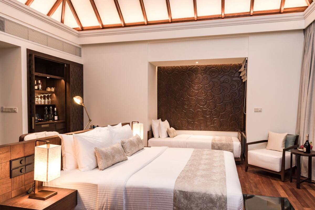 Quarto de hotel com duas camas, um minibar, uma escrivaninha com candeeiro e uma cabeceira decorativa.