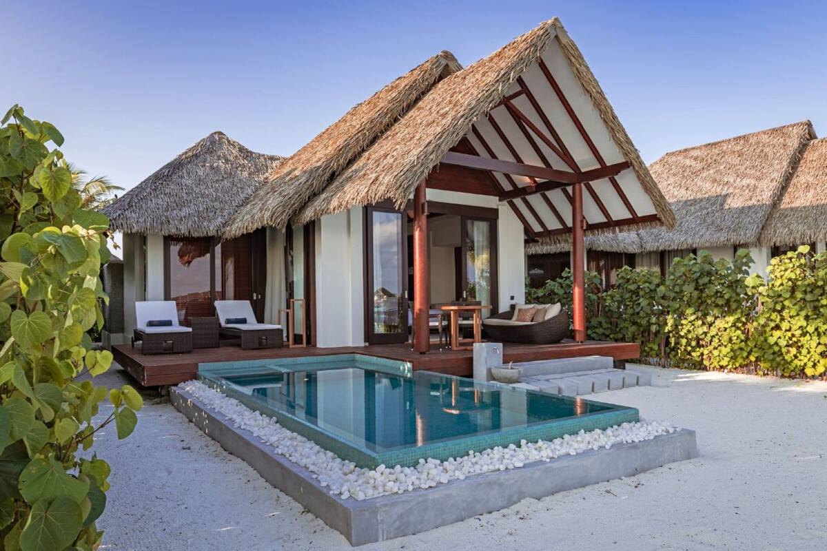 Um resort com villas de telhado de palha, piscina e praia de areia.