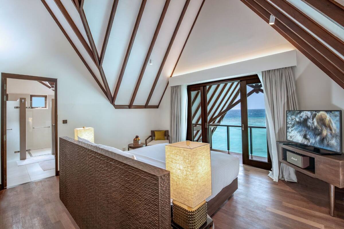 Quarto de hotel moderno com uma cama grande, televisão, vista para o mar e varanda.