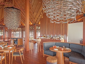 A spacious restaurant with wooden beams, a high ceiling, and a bar area with various food and drink displays. - Heritance Aarah (Aarah)