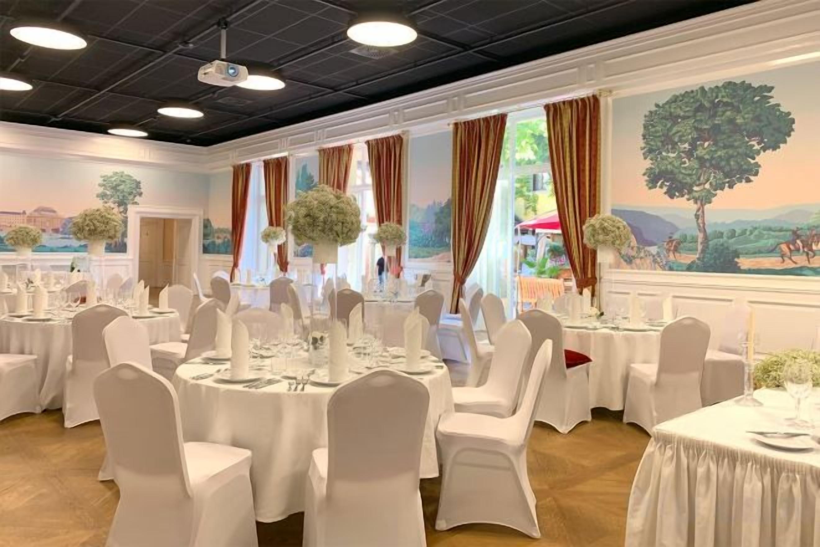 A banquet hall with round tables, white chairs, and floral centerpieces.