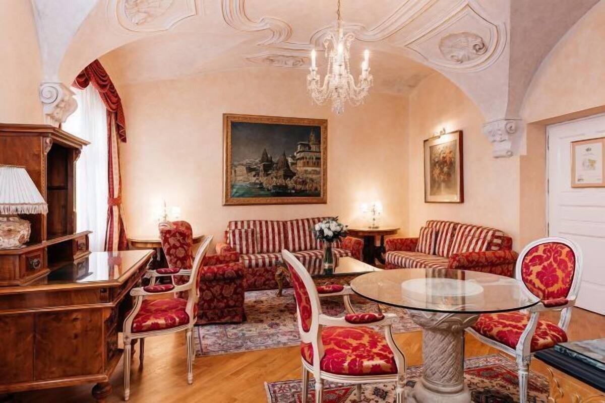Une pièce avec une table ronde en verre, des canapés à motifs rouges et un lustre.