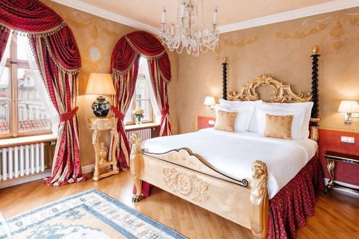 Une chambre à coucher classique, avec un lit à baldaquin, une tête de lit décorée et des rideaux rouges.