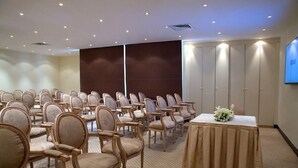 A conference room with rows of chairs, a table with a white tablecloth, and a television screen on the wall. - Inn And Go Kuwait Plaza Hotel (Kuwait City)