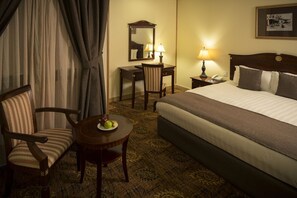 A hotel room with a bed, a desk, a chair, a small table with fruit, and a lamp. - Inn And Go Kuwait Plaza Hotel (Kuwait City)