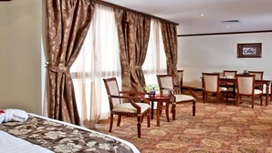 A hotel room with a bed, a dining area with chairs and a table, and a large window with curtains. - Inn And Go Kuwait Plaza Hotel (Kuwait City)