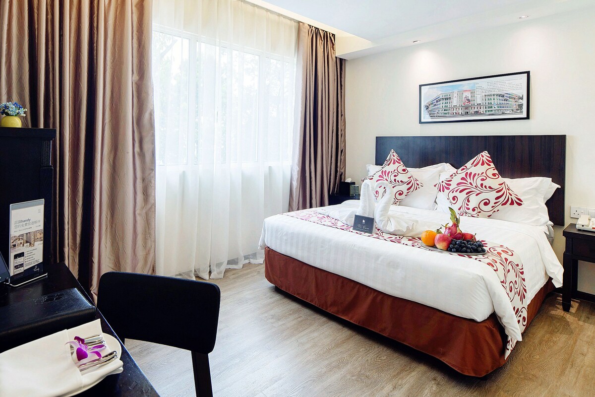 Habitación de hotel con cama, escritorio con computadora, silla y mesita de noche con teléfono.