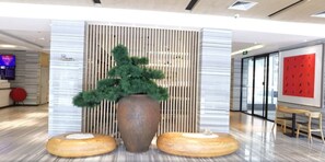 A reception area with a large potted plant, a wooden slat wall, and a digital display. - Ji Hotel (Xiamen)