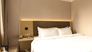 A hotel room with a bed, bedside table, and a wall-mounted light fixture. - Ji Hotel (Xiamen)