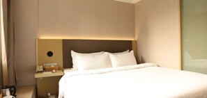 Ein Hotelzimmer mit einem ordentlich bezogenen Bett, einem Nachttisch mit Lampe und einer Wandleuchte.
