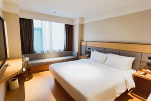 A hotel room with a large bed, a bedside table, a desk, a chair, a window with curtains, and a view of the outside. - Ji Hotel (Xiamen)