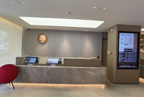 A reception area with a marble counter, digital information screens, and a red chair. - Ji Hotel (Xiamen)