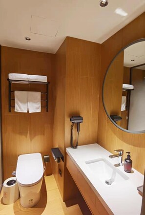 Un baño moderno con tocador de madera, un espejo redondo, inodoro y perchero para toallas.