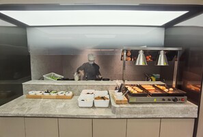 A commercial kitchen with a chef preparing food, a grill, and various food containers on the counter. - Ji Hotel (Xiamen)