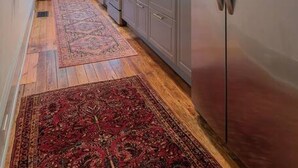 Une cuisine moderne avec des meubles gris, un réfrigérateur en acier inoxydable et un tapis rouge à motifs.