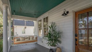 Une véranda avec une balançoire en bois, une plante en pot et une porte.