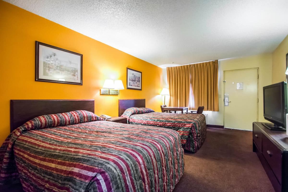 A hotel room with two beds, a television, a desk, and two lamps.