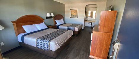 A hotel room with two beds, a desk, a chair, a mirror, and a refrigerator.