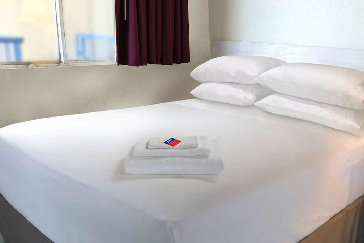 A neatly made bed with white linens, a folded towel, and a pillow.