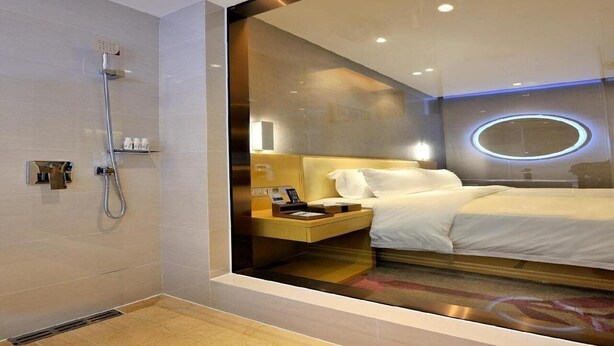 A modern hotel room with a shower, a bedside table with a phone, and a bed with white bedding.
