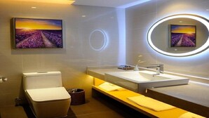 A modern bathroom with a toilet, sink, and a large mirror with a circular light. There are two framed pictures on the wall.