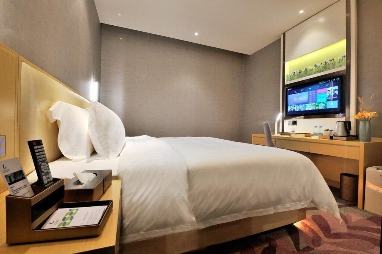 Une chambre d’hôtel moderne dotée d’un grand lit, d’un bureau avec un ordinateur et une télévision à écran plat, ainsi que d’un grand miroir au-dessus du bureau.