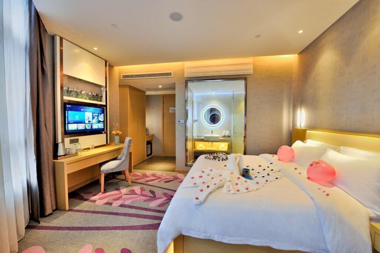 Een hotelkamer met een bed, een bureau met een televisie, een stoel, een badkamer met een spiegel en een douche.