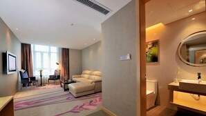 A hotel room with a living area featuring a sofa, chairs, and a coffee table. There is a bathroom with a sink and toilet.