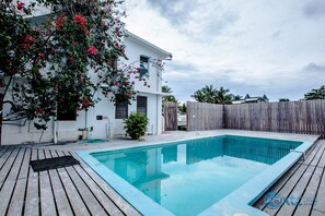 Enjoy a refreshing dip in the pool surrounded by a wooden deck and lush palm trees.