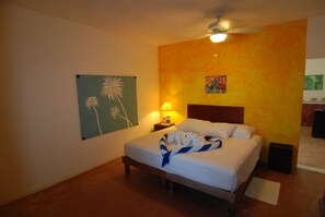 Relax in a cozy space with a single bed against a bold wall, a ceiling fan above and a table with a lamp nearby.